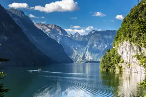 Ein Boot fährt auf einem ruhigen See, umgeben von steilen, bewaldeten Bergen. Ein idyllisches Bild von Badeseen Deutschland.