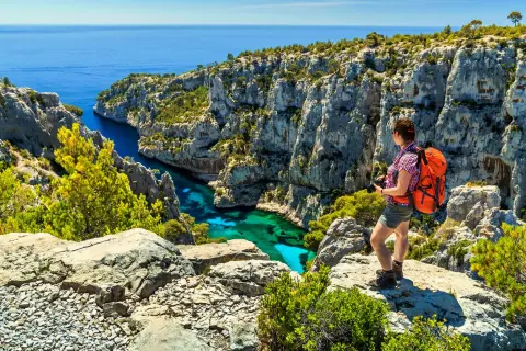 Frau mit Rucksack genießt den Ausblick beim Marseille Wandern. Türkisblaues Wasser in einer Felsbucht.