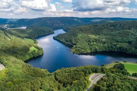 Idyllische Seenlandschaft in der Eifel mit kurviger Straße und einem Schiff. Entdecken Sie diese Eifel Geheimtipps!