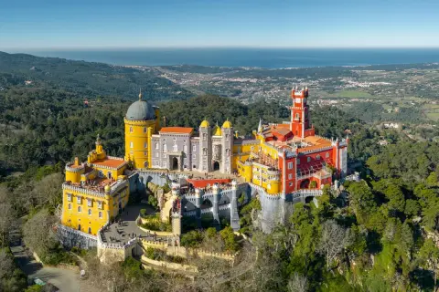 Buntes Schloss Pena thront auf Hügel, mit Blick auf das Meer. Ein grünes Auto parkt am sintra parking Weg.