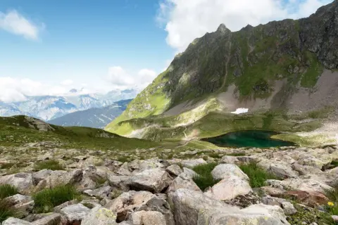 Bergsee bei Schruns, ideal zum Wandern. Grüne Hänge, Felsen und ein tiefblauer Bergsee unter blauem Himmel.