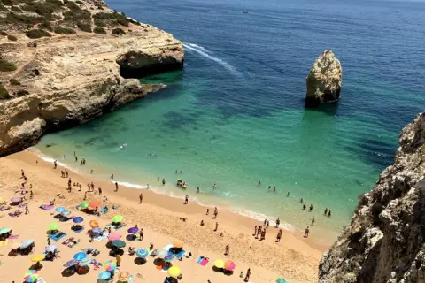 Sonniger Strand an der Algarve, ein echter Geheimtipp mit türkisfarbenem Wasser, Felsen und vielen bunten Sonnenschirmen.