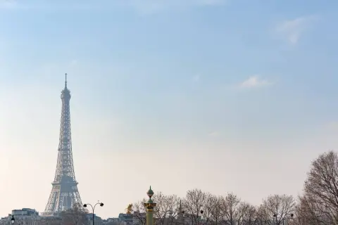 Eiffelturm ragt im winterlichen Paris in den blauen Himmel. Kahle Bäume säumen die Stadt.