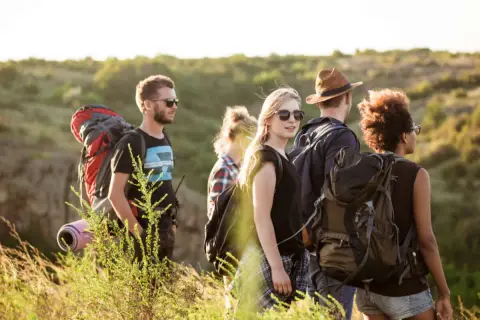 Eine Gruppe junger Leute lernt wandern. Sie tragen Rucksäcke und genießen die Natur bei Sonnenschein.