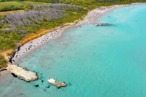 Traumhafter Strand in Apulien mit türkisfarbenem Wasser, sonnenhungrigen Menschen und grünen Hügeln im Hintergrund.