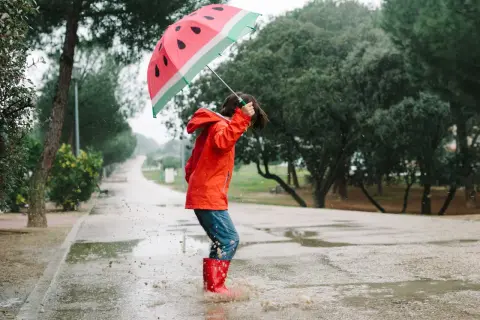 Kind mit Regenschirm und Gummistiefeln springt in Pfütze. Perfekte Freizeit NRW für Regentage.