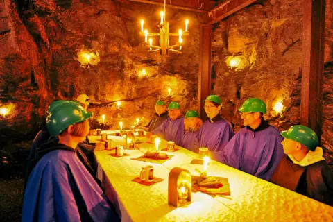 Festlich gedeckter Tisch im Bergwerk Annaberg. Gäste in Schutzhelmen und Umhängen speisen bei Kerzenlicht in der Felsenkammer.