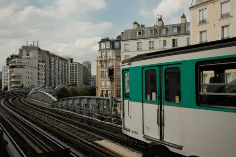 Ein Pariser Métro-Zug fährt auf den Gleisen in Richtung Saint-Lazare. Gebäude und eine Brücke säumen die Strecke.