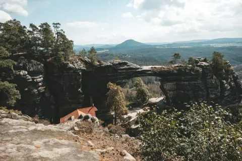 Felsentor in Böhmischer Schweiz, nahe dem Erzgebirge Tschechien. Ein malerischer Ausblick auf bewaldete Hügel und eine kleine Hütte.
