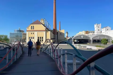 Zwei Personen spazieren über eine Brücke zur Pilsner Brauerei. Ein Geheimtipp für Bierliebhaber!
