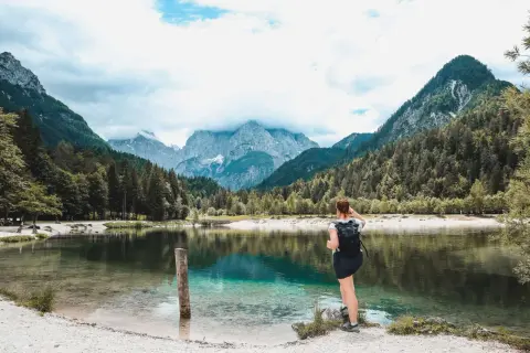 Frau mit Rucksack genießt den Ausblick auf den Jasna See und die Berge. Perfekt für Kranjska Gora Wandern.