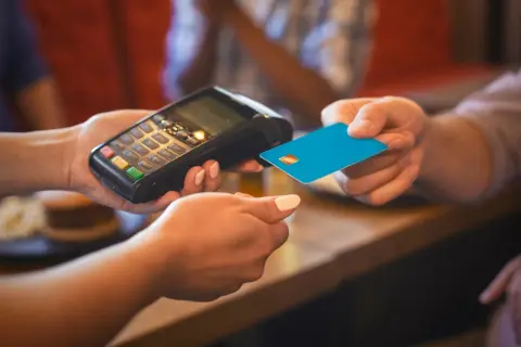 Eine Person bezahlt mit einer blauen Karte an einem Terminal. Das ist eine typische Transaktion, wenn man in Frankreich Geld ausgibt.