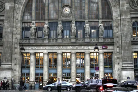 Prachtvolle Fassade des **Paris Nord Bahnhof** mit Statuen und einer Uhr. Autos und Menschen beleben den Vorplatz.