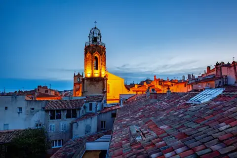 Aix-en-Provence Geheimtipps: Ein beleuchteter Kirchturm ragt über die Dächer der Altstadt im Abendlicht.