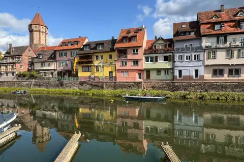 Bunte Häuserfront am Flussufer, ein Turm ragt empor. Hier könnte das Taubertal sein, mit Spiegelungen im Wasser.