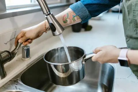 Eine Hand dreht den Wasserhahn auf, um einen Topf mit Leitungswasser aus Budapest zu füllen.