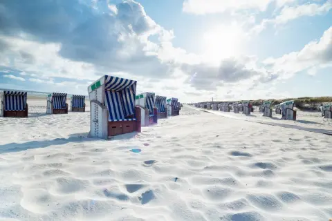 Strandkörbe auf einer autofreien ostfriesischen Insel. Sonnenschein und Wolken über dem weißen Sand.