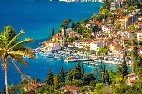 Bunte Häuser am Meer, Boote im Hafen und eine Palme – ein malerischer Blick auf Opatija, der Lust auf Entdeckungen macht. Hier gibt es viele Opatija Geheimtipps zu entdecken.