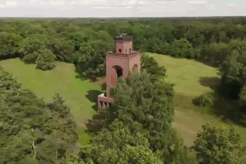 Ein roter Backsteinturm ragt aus einer grünen Wiese im Spreewald, umgeben von üppigen Bäumen.