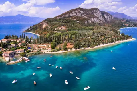 Punta San Vigilio: malerische Halbinsel mit historischen Gebäuden, Olivenhainen und dem türkisfarbenen Gardasee, belebt durch zahlreiche Boote.