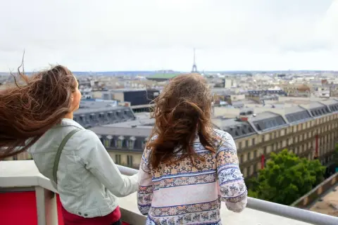 Zwei Teenager genießen den Blick über Paris. Der Wind spielt mit ihren Haaren, während sie die Stadt und den Eiffelturm bestaunen.