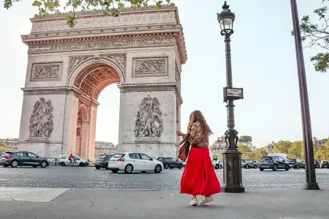 Frau in rotem Kleid tanzt vor dem Arc de Triomphe in Paris.