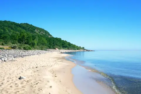 Sandstrand mit Felsen und grünen Hügeln, ein Highlight der schwedischen Landschaft.