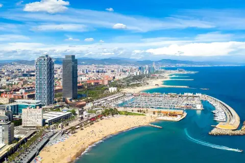 Blick auf den belebten barcelona strand mit Yachten im Hafen und der Skyline der Stadt im Hintergrund.