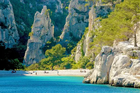 Sonnige Bucht mit türkisfarbenem Wasser und Felsen, ideal zum Calanques Baden. Menschen entspannen am Strand.