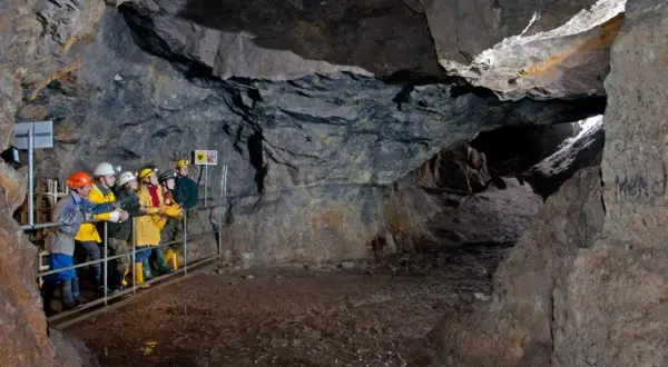 Besucher erkunden eine Höhle im Erzgebirge. Sie tragen Schutzhelme und blicken in die Tiefe des Bergwerks.