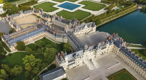 Luftaufnahme des prächtigen Schlosses Fontainebleau mit seinen weitläufigen Höfen, Gärten und einem See.