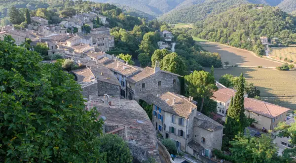 Dächer und Steinhäuser eines Dorfes im Luberon, Provence, eingebettet in grüne Hügel und Felder.