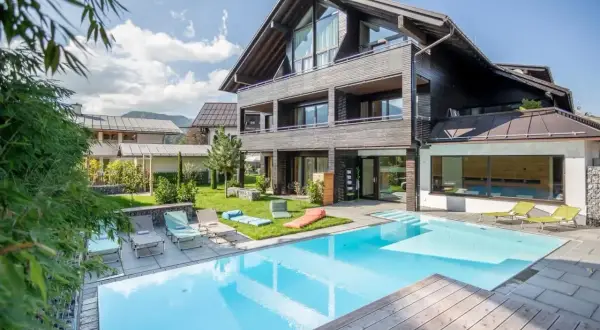 Moderner Poolbereich mit Liegestühlen und Blick auf ein stilvolles Holzhaus. Hier finden Sie die besten Oberstdorf Geheimtipps für Ihren Urlaub.
