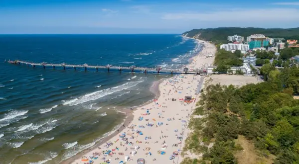 Blick auf die belebte Misdroy Promenade mit Strand, Meer und Seebrücke. Viele Menschen genießen den sonnigen Tag am Ostseestrand.