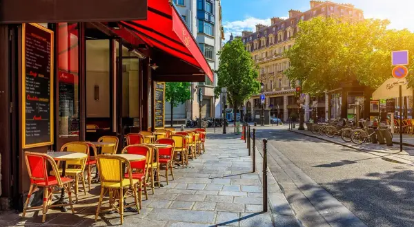 Ein sonniger Tag in Oberkampf, Paris. Rote und gelbe Stühle laden vor einem Café zum Verweilen ein.