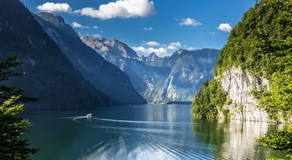 Ein Boot fährt auf einem ruhigen See, umgeben von steilen, bewaldeten Bergen. Ein idyllisches Bild von Badeseen Deutschland.