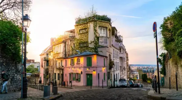 Malerische Gasse in Paris, perfekt für Sightseeing. Ein rosa Restaurant mit grünen Fensterläden und ein Mann mit Maske auf dem Kopfsteinpflaster.