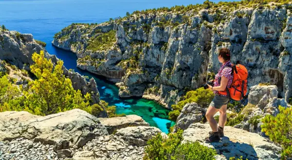 Frau mit Rucksack genießt den Ausblick beim Marseille Wandern. Türkisblaues Wasser in einer Felsbucht.