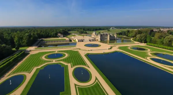 Das Chantilly Schloss mit seinen symmetrischen Wasserbecken und gepflegten Gärten, umgeben von einem weitläufigen Wald.