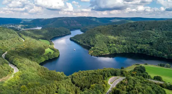 Idyllische Seenlandschaft in der Eifel mit kurviger Straße und einem Schiff. Entdecken Sie diese Eifel Geheimtipps!