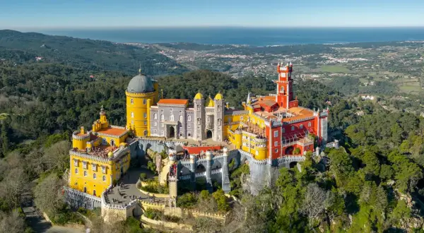 Buntes Schloss Pena thront auf Hügel, mit Blick auf das Meer. Ein grünes Auto parkt am sintra parking Weg.