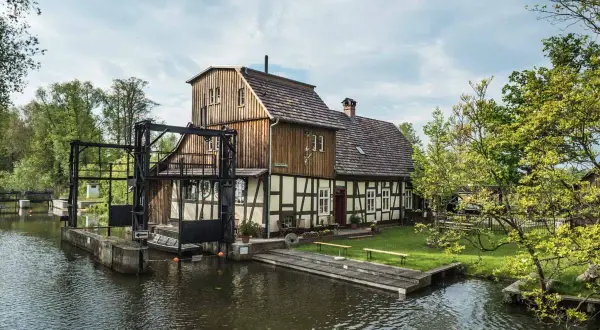 Historische Wassermühle am Wasser, perfekt für einen Spreewald Tagesausflug. Ein idyllischer Ort mit viel Grün und Wasser.