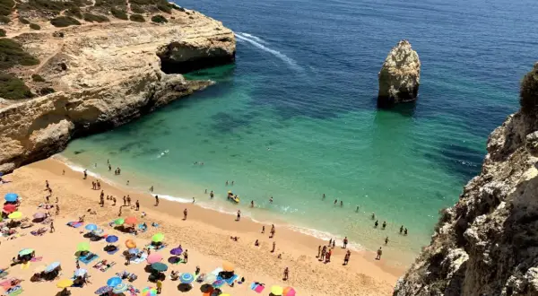 Sonniger Strand an der Algarve, ein echter Geheimtipp mit türkisfarbenem Wasser, Felsen und vielen bunten Sonnenschirmen.