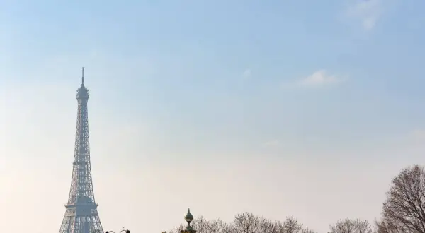 Eiffelturm ragt im winterlichen Paris in den blauen Himmel. Kahle Bäume säumen die Stadt.