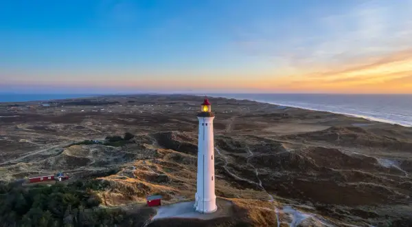 Leuchtturm bei Sonnenuntergang an der Küste, umgeben von Dünen. Ein versteckter Ort, der an Hvide Sande Geheimtipps erinnert.