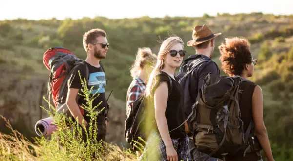 Eine Gruppe junger Leute lernt wandern. Sie tragen Rucksäcke und genießen die Natur bei Sonnenschein.