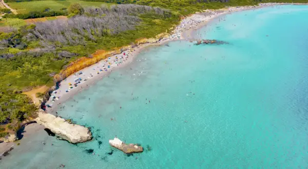 Traumhafter Strand in Apulien mit türkisfarbenem Wasser, sonnenhungrigen Menschen und grünen Hügeln im Hintergrund.