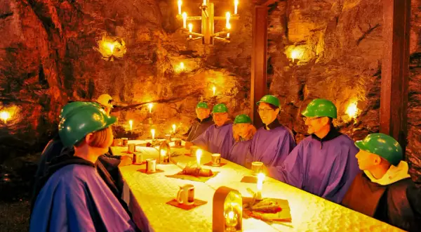 Festlich gedeckter Tisch im Bergwerk Annaberg. Gäste in Schutzhelmen und Umhängen speisen bei Kerzenlicht in der Felsenkammer.