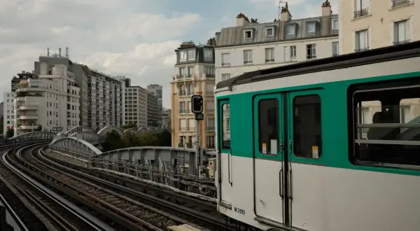 Ein Pariser Métro-Zug fährt auf den Gleisen in Richtung Saint-Lazare. Gebäude und eine Brücke säumen die Strecke.