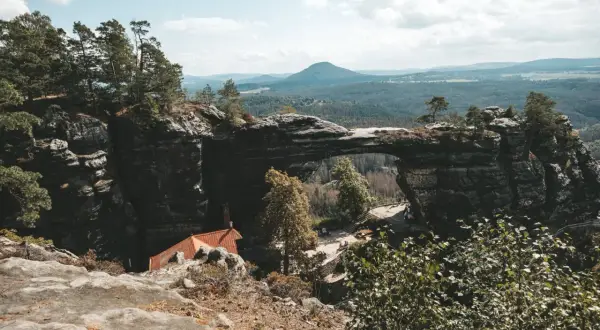 Felsentor in Böhmischer Schweiz, nahe dem Erzgebirge Tschechien. Ein malerischer Ausblick auf bewaldete Hügel und eine kleine Hütte.